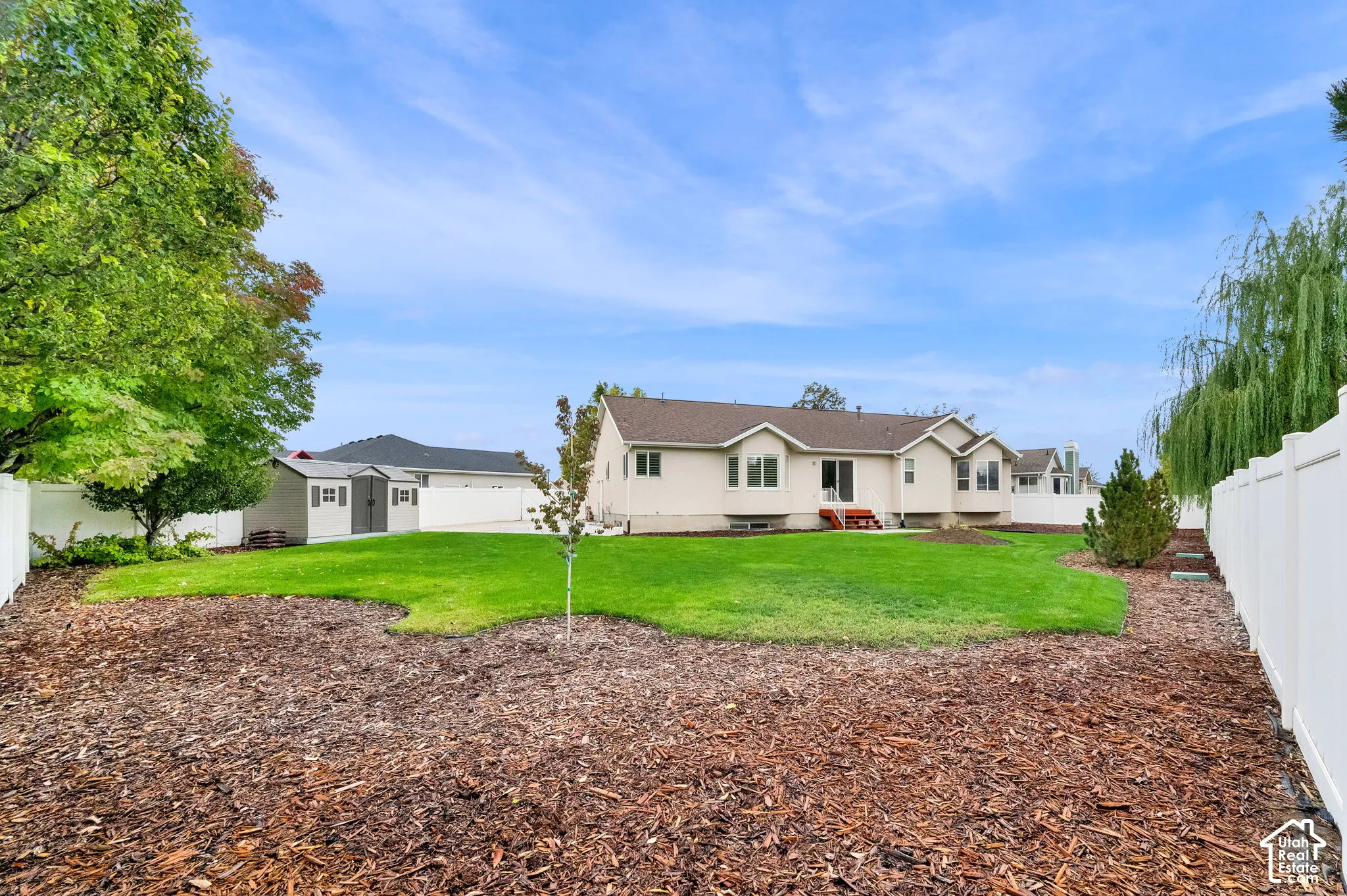Backyard featuring a manicured lawn, wood mulch landscaping, white vinyl perimeter fencing, and a detached storage shed