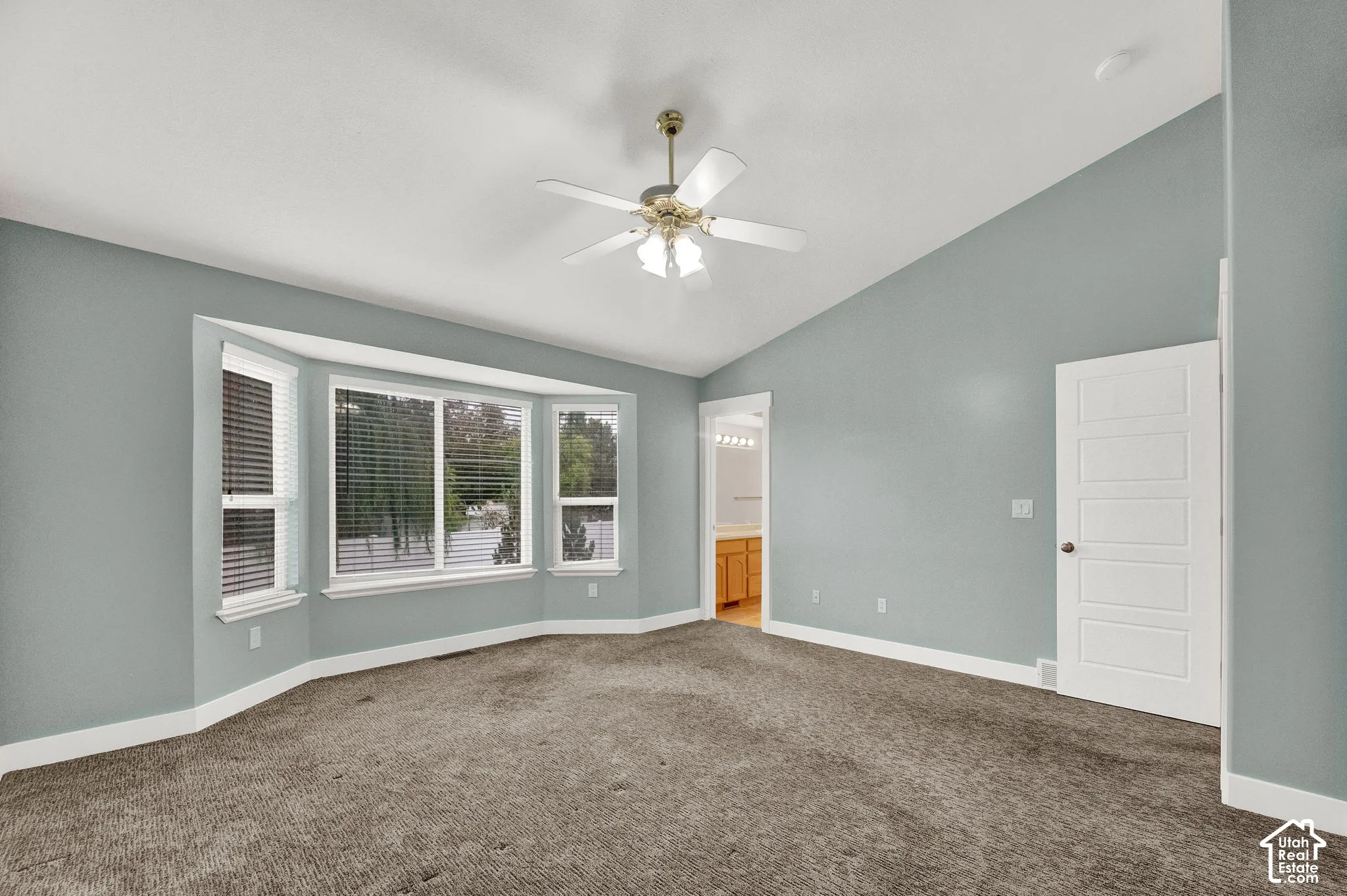 Room featuring a vaulted ceiling, bay window, carpeted flooring, a ceiling fan with integrated lighting, and a five-panel interior door