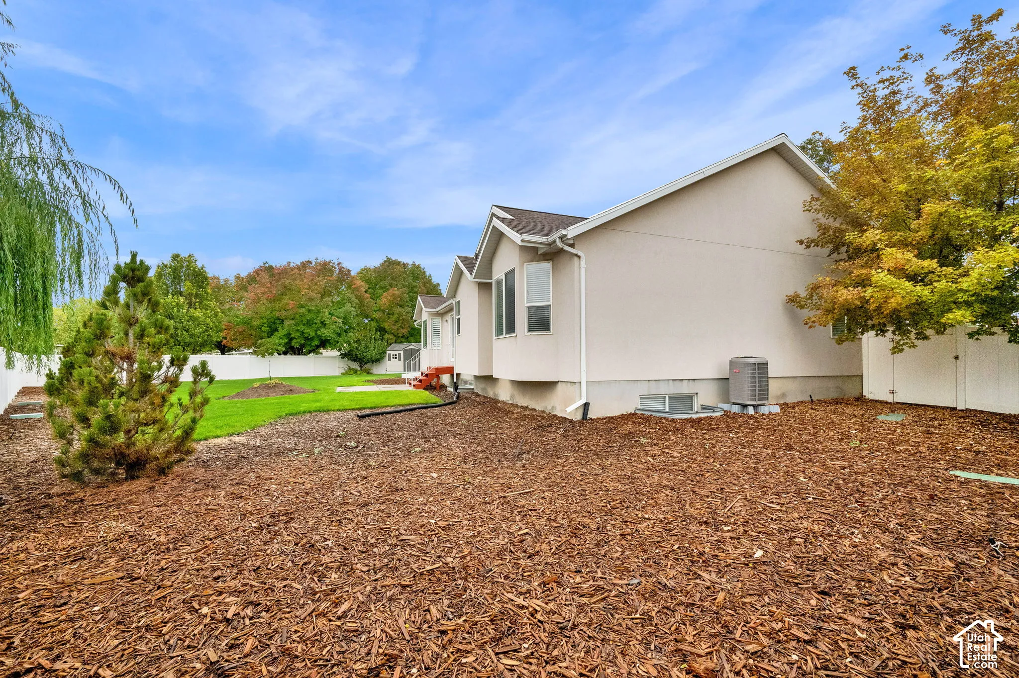 Exterior featuring a multi-gabled roofline, light-toned siding, white vinyl perimeter fencing, and a mulched ground cover