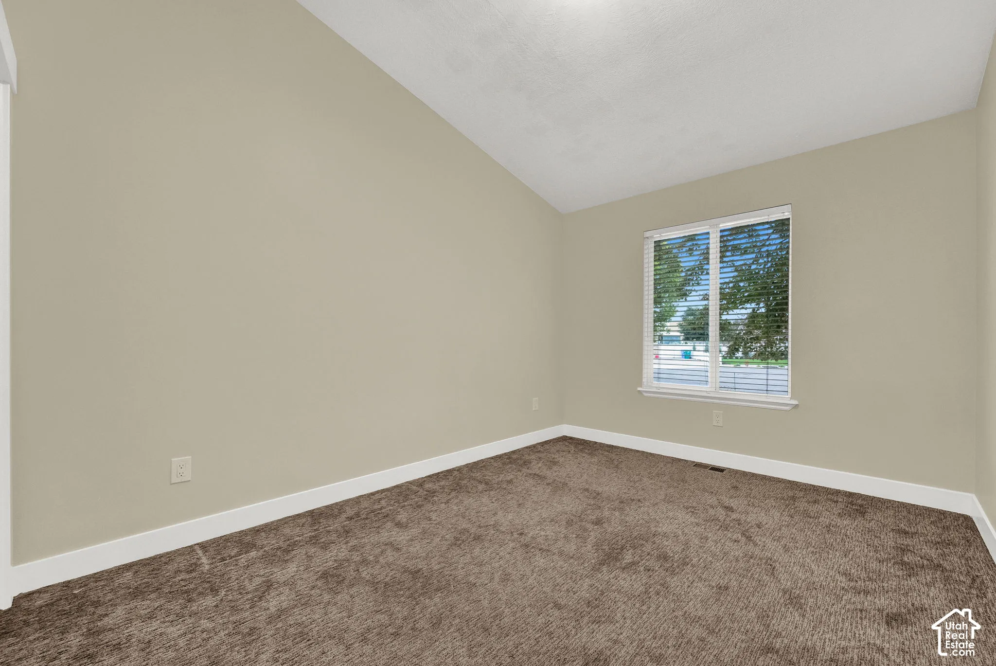 Room featuring vaulted ceilings, neutral wall tones, wall-to-wall carpeting, and a double-pane window with integrated blinds