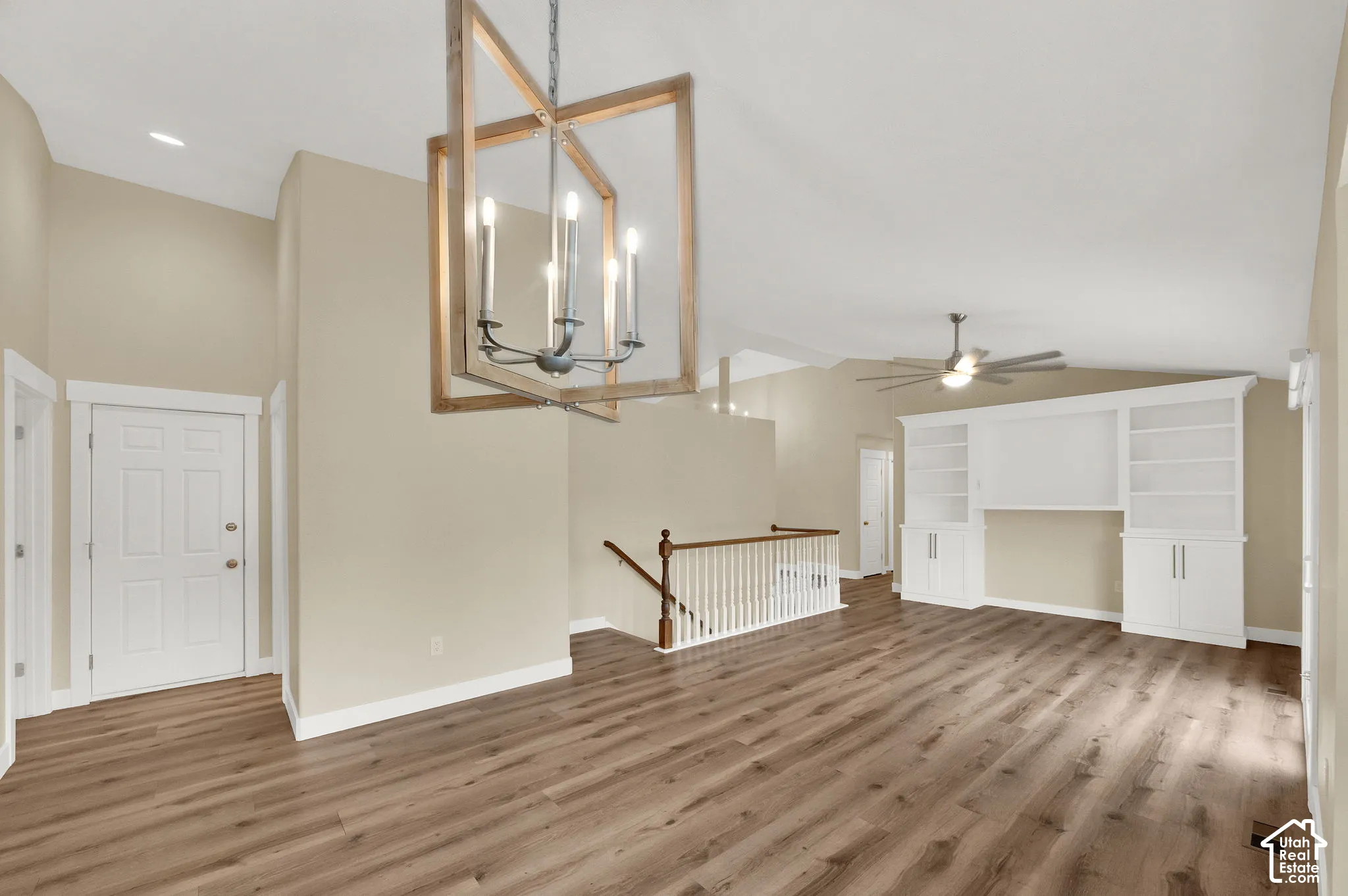 Vaulted ceilings, wood-finish flooring, built-in shelving, decorative metal and wood-frame chandelier, and a white painted handrail with balusters