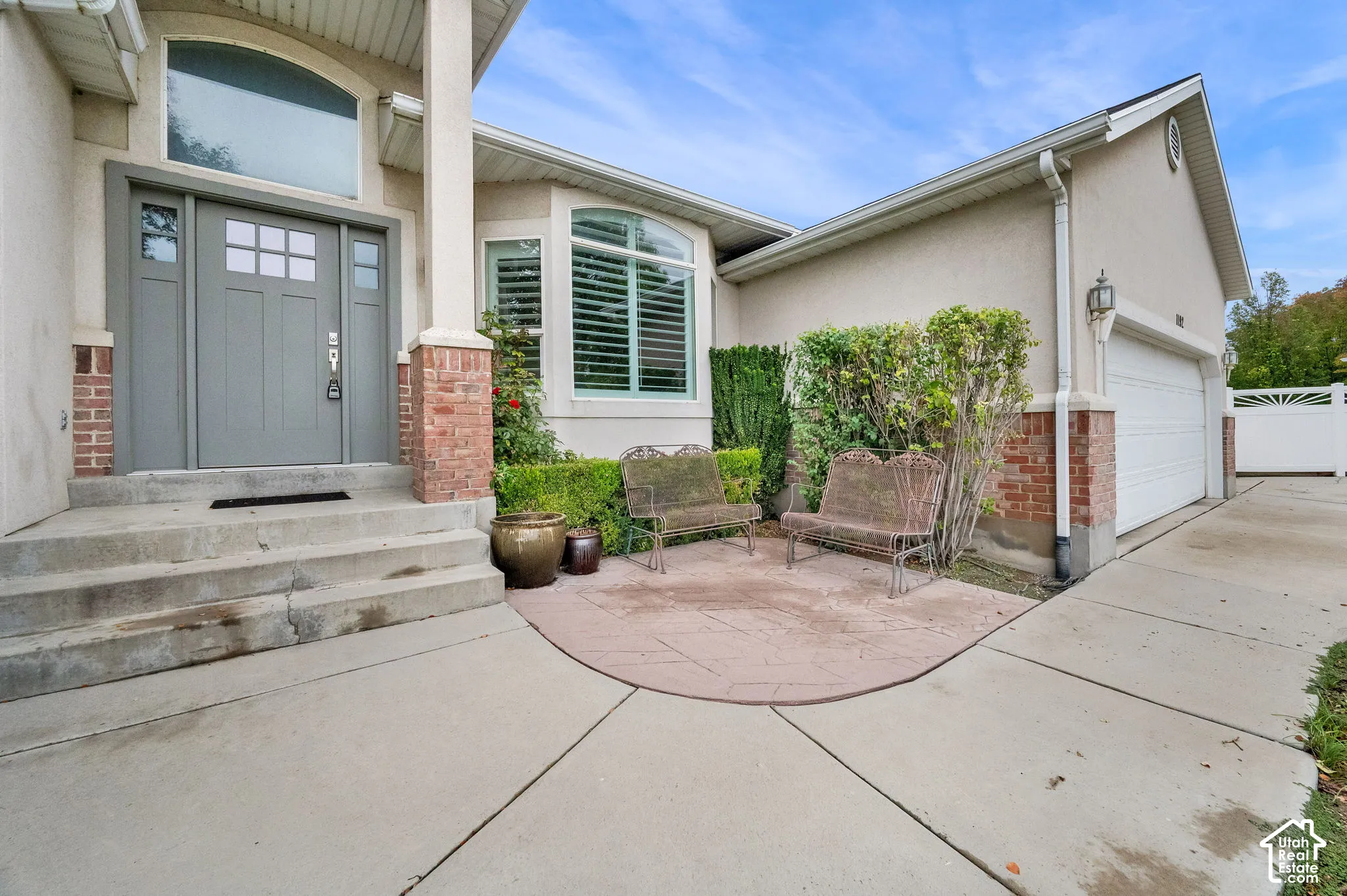Exterior facade featuring stucco siding with brick veneer accents, arched windows, a multi-panel front door with sidelights, and a decorative concrete front patio