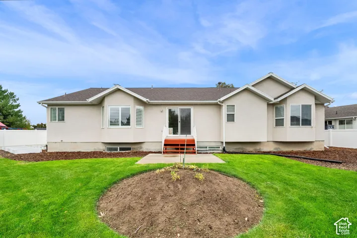 Exterior rear elevation featuring stucco siding, double-pane bay windows, a concrete patio, wood-finished stairs, and a white privacy fence