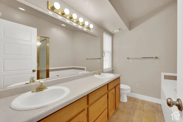 Double vanity featuring oval drop-in sinks, a full-width mirror, wood cabinetry, and a tiered soaker tub