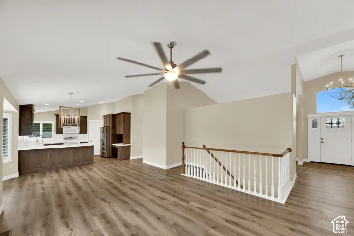 Vaulted ceilings featuring a multi-blade ceiling fan, wood-finish flooring, white staircase railing with a wood handrail, and built-in cabinetry