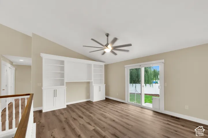 Vaulted ceiling, wood-finish flooring, built-in white cabinetry with shelving, multi-blade ceiling fan, and sliding glass door