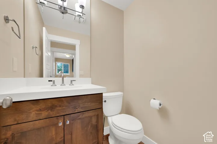 Wood-finish cabinetry paired with a white countertop and integrated sink, chrome faucet hardware, wall-mounted light fixture, and large rectangular vanity mirror