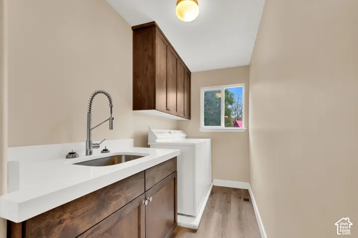 Laundry area featuring wood-finish cabinetry, white countertop, undermount sink with a gooseneck faucet, and wood-finish flooring