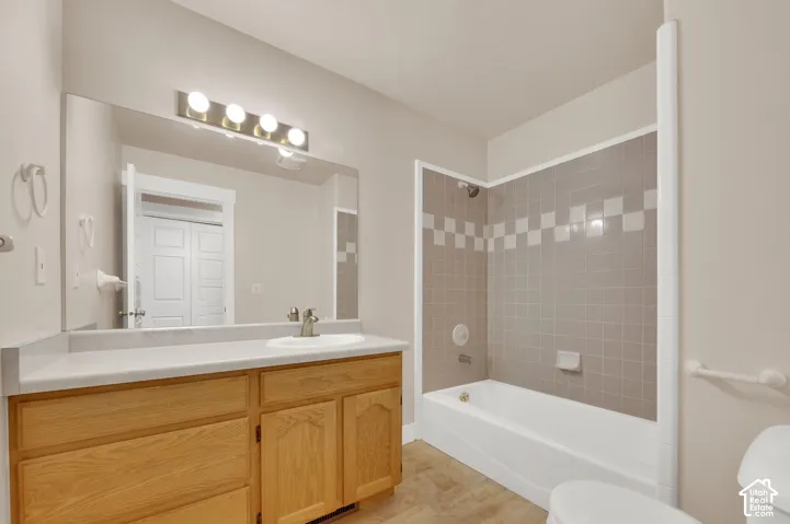 Bathroom featuring a wood-finish vanity with a light-toned countertop, a full-width wall mirror, a five-light fixture, and a tub-shower combination with decorative tile surround