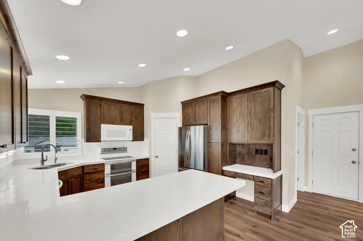 Kitchen featuring dark-stained wood cabinetry, white countertops, stainless steel appliances, a built-in workspace, and wood-finish flooring