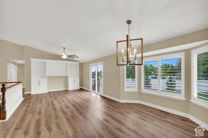 Wood-finish flooring, built-in white cabinetry, geometric pendant lighting, sliding glass door, and bay window featuring plantation shutters