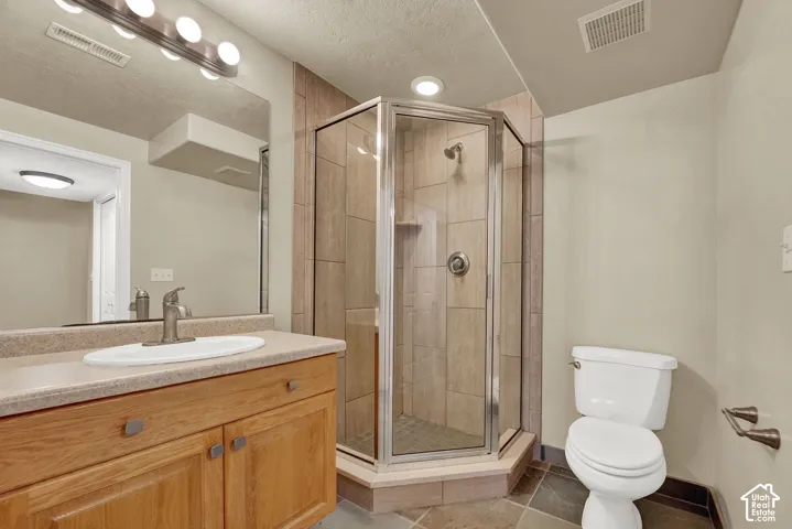 Wood vanity featuring a solid surface countertop with an integrated basin, corner glass-enclosed shower with tile surround, and tile flooring