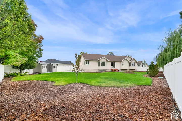 Backyard featuring a manicured lawn, wood mulch landscaping, white vinyl perimeter fencing, and a detached storage shed