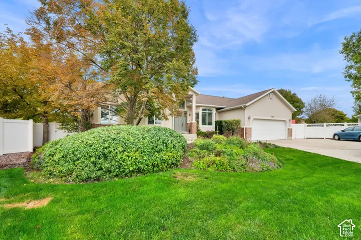 Single-story exterior featuring a light-toned stucco and brick facade, an attached two-car garage, an arched entryway, and perimeter white vinyl fencing