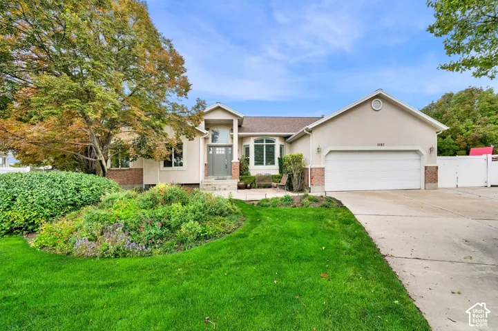 Single-story exterior featuring a stucco and brick facade, an arched entryway, a large multi-pane bay window, and a multi-car concrete driveway
