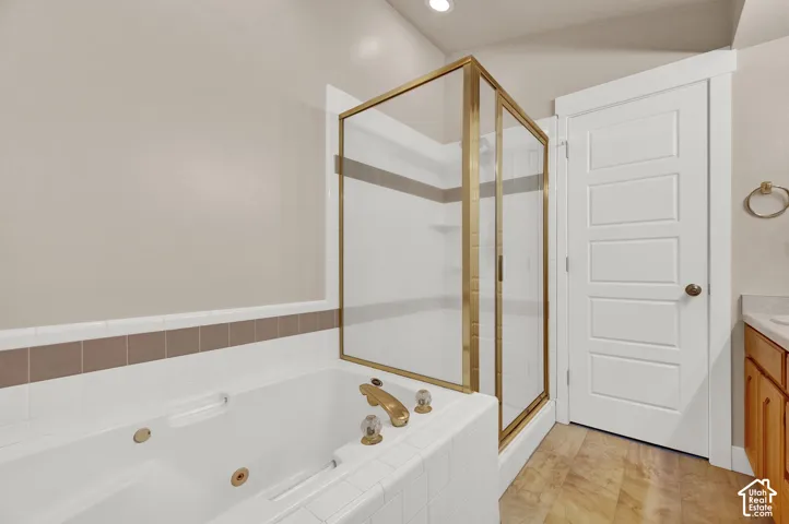 Jetted soaking tub with tile surround, glass-enclosed shower with gold-tone frame, and wood-finish flooring