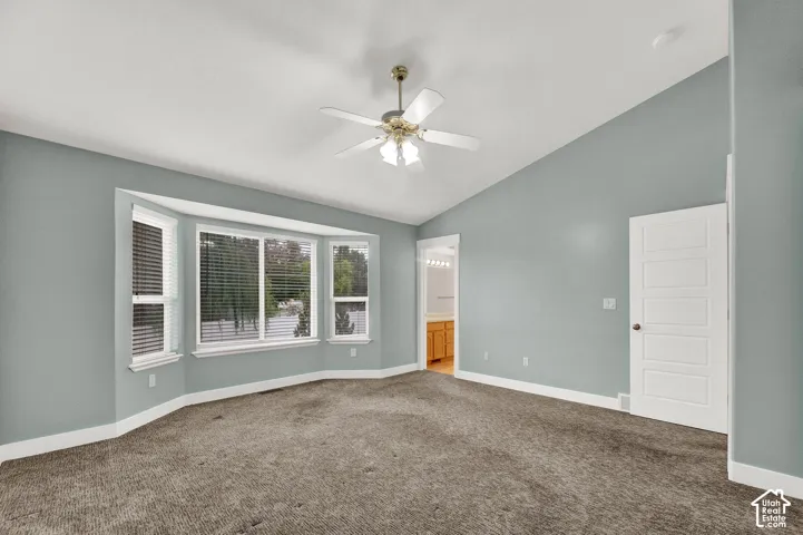 Room featuring a vaulted ceiling, bay window, carpeted flooring, a ceiling fan with integrated lighting, and a five-panel interior door
