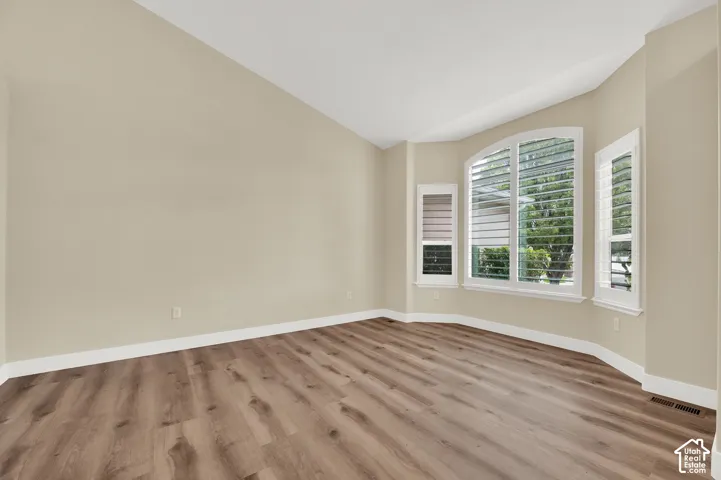 Vaulted ceilings, wood-finish flooring, and a bay window featuring arched casing and integrated plantation shutters