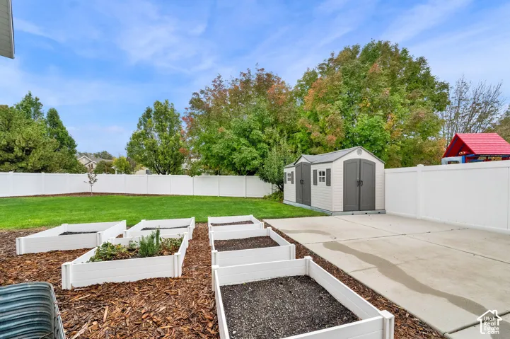 Private backyard featuring a concrete patio, multiple elevated garden beds, a detached resin storage shed, and full vinyl privacy fencing