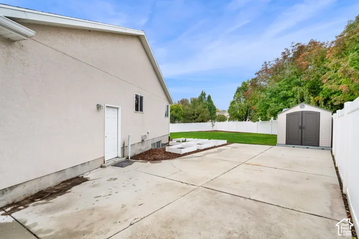 Backyard featuring a concrete parking pad, white vinyl perimeter fencing, raised garden beds, and a detached storage shed