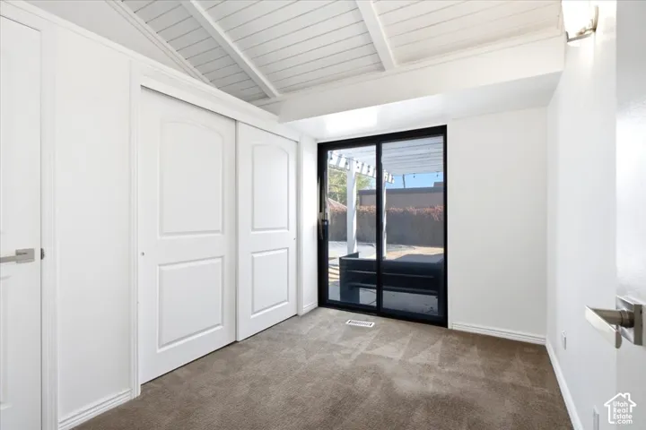 Vaulted ceiling with exposed beams, sliding glass door with black frame, built-in closet with multi-panel doors, and wall-mounted lighting fixture