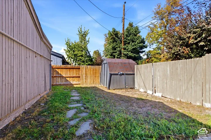 Exterior area featuring a wood-panel fence, a standalone storage shed, and a stone paver path
