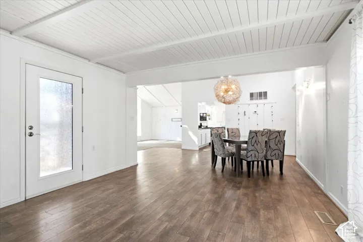 Wood-finish flooring throughout with vaulted ceilings featuring exposed beams, a textured glass-paneled exterior door, and a spherical metallic pendant light fixture