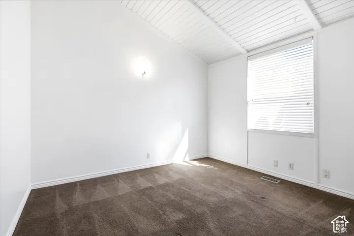 Vaulted ceiling with exposed beams, neutral carpeting, and a window with horizontal blinds