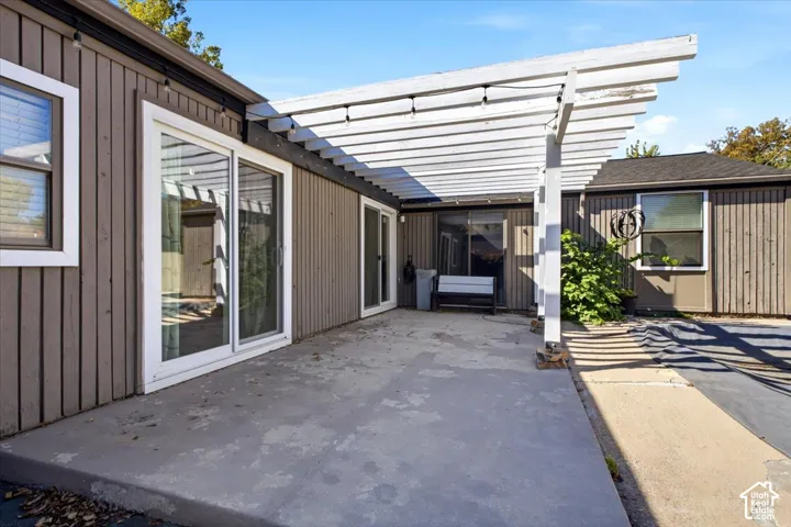 Concrete patio featuring a white wood-frame pergola, vertical composite siding, and dual sliding glass doors