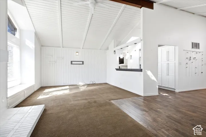 Vaulted ceilings with exposed beams, wood-finish flooring, vertical plank wall detailing, built-in window seat, and a pass-through bar counter with pendant lighting
