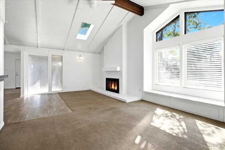 Vaulted ceiling with exposed wood beam, skylight, fireplace with masonry surround, expansive multi-panel windows, and integrated built-in bench seating