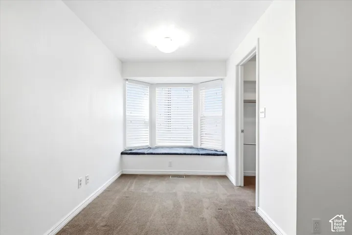Bay window with integrated bench seating, neutral carpeting, and a walk-in closet