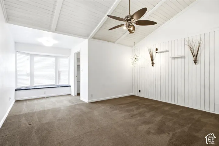 Vaulted ceiling with exposed beams, bay window featuring a built-in bench, vertical wall paneling, and a central ceiling fan