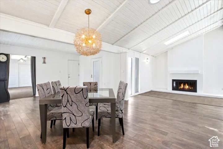 Vaulted ceiling with exposed beams, wood-finish flooring, built-in fireplace with a minimalist mantel, skylight, and decorative globe pendant lighting