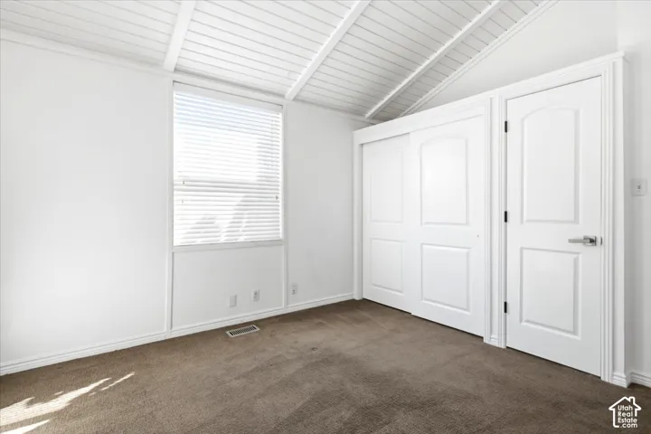 Vaulted ceiling with exposed beams, paneled door closet, interior passage door, and neutral carpeting