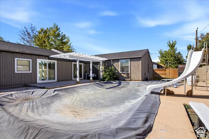 Backyard featuring a covered patio with a white pergola, swimming pool with a slide, and vertical exterior siding