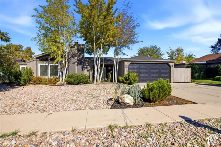 Single-story exterior featuring dark-toned siding, an attached two-car garage, an integrated stone-finish chimney, and low-maintenance rock landscaping