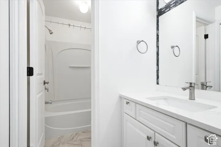 Bathroom featuring a vanity with stone-finish countertop, undermount sink, brushed nickel faucet, large wall mirror with dark tile accents, and a tub-shower combination with molded surround