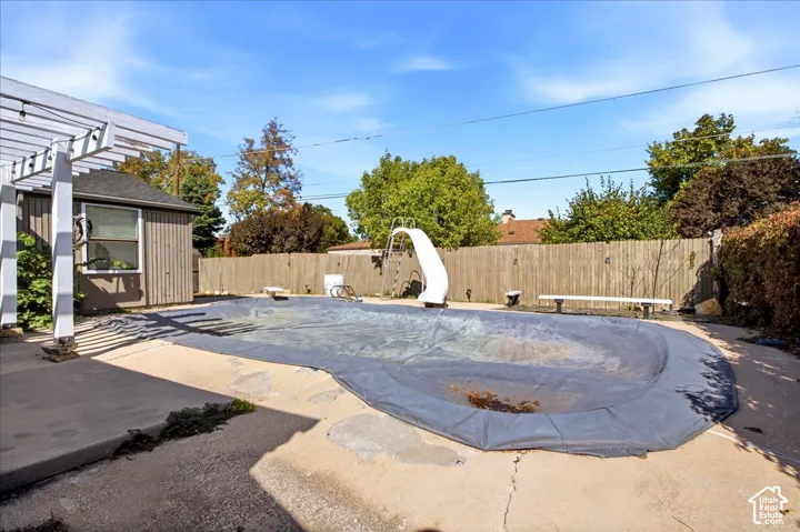 Outdoor living space featuring an inground pool with a slide, a white pergola, and wooden privacy fencing