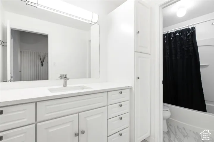 Bathroom featuring white cabinetry with a vanity, tall built-in storage, integrated rectangular sink, wall-spanning mirror, and stone-pattern flooring