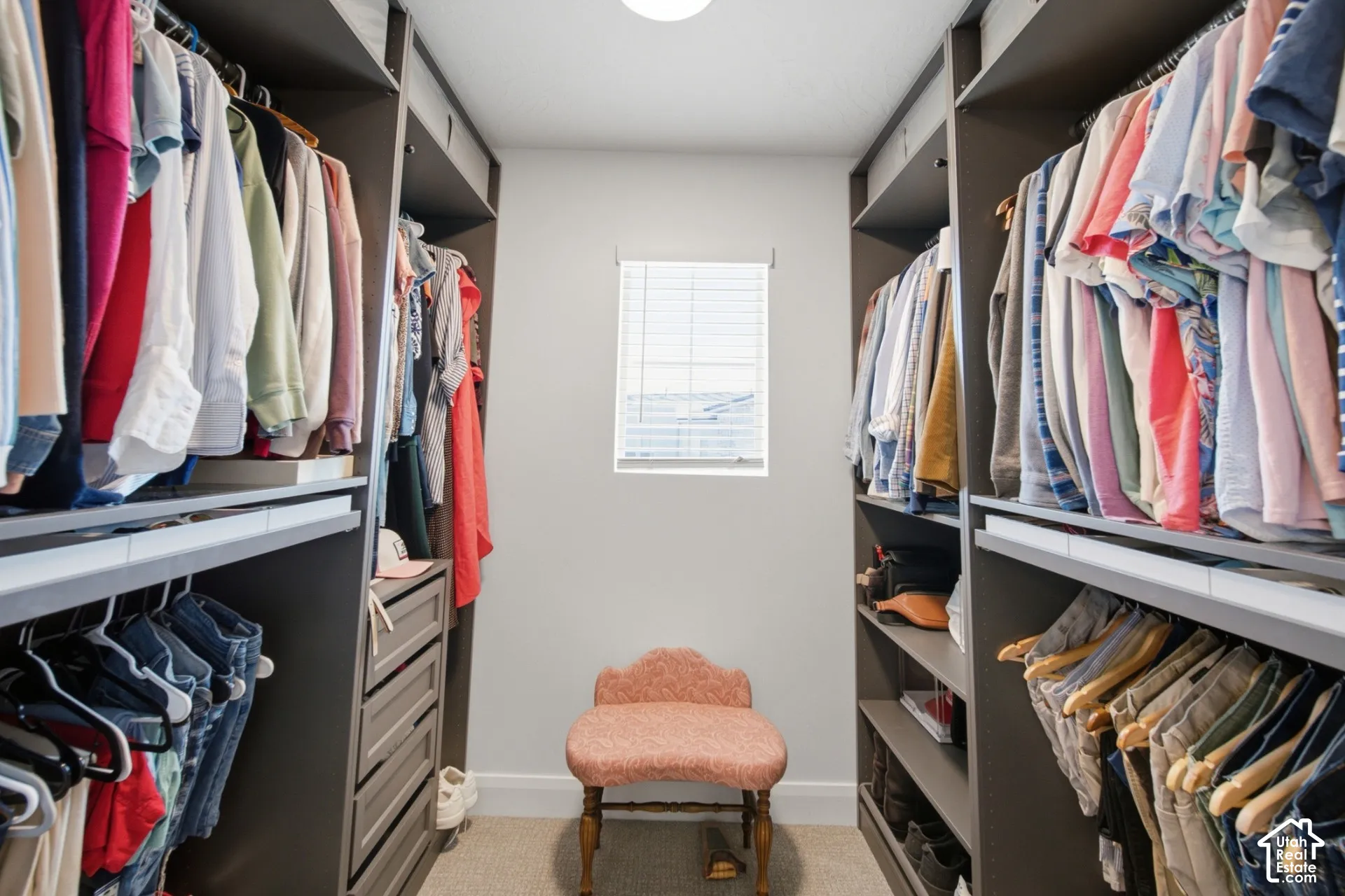 Walk-in closet featuring custom built-in dark cabinetry, integrated shelving units, tiered hanging rods, and a window with neutral-toned blinds