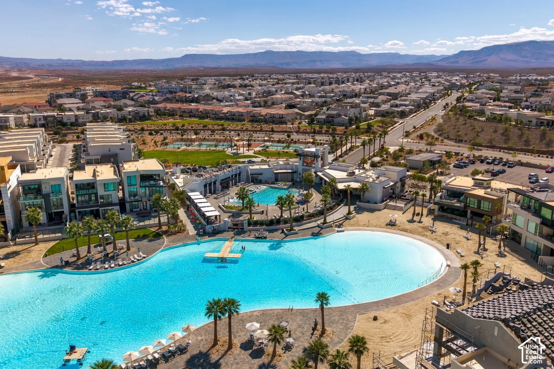 Large-scale recreational lagoon with perimeter paving, palm tree landscaping, clubhouse, community pool, and mountain backdrop