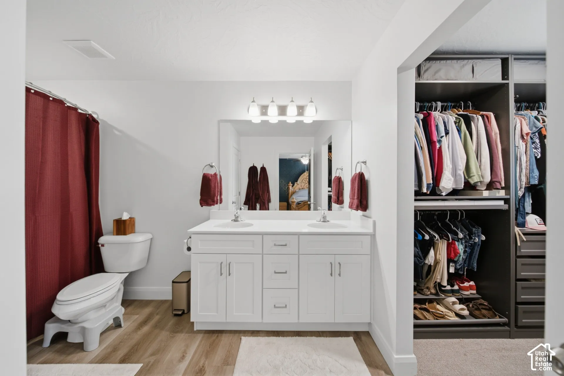 Bathroom featuring a white double-sink vanity with a solid-surface countertop, full-width vanity mirror, integrated wall lighting, and wood-finish flooring
