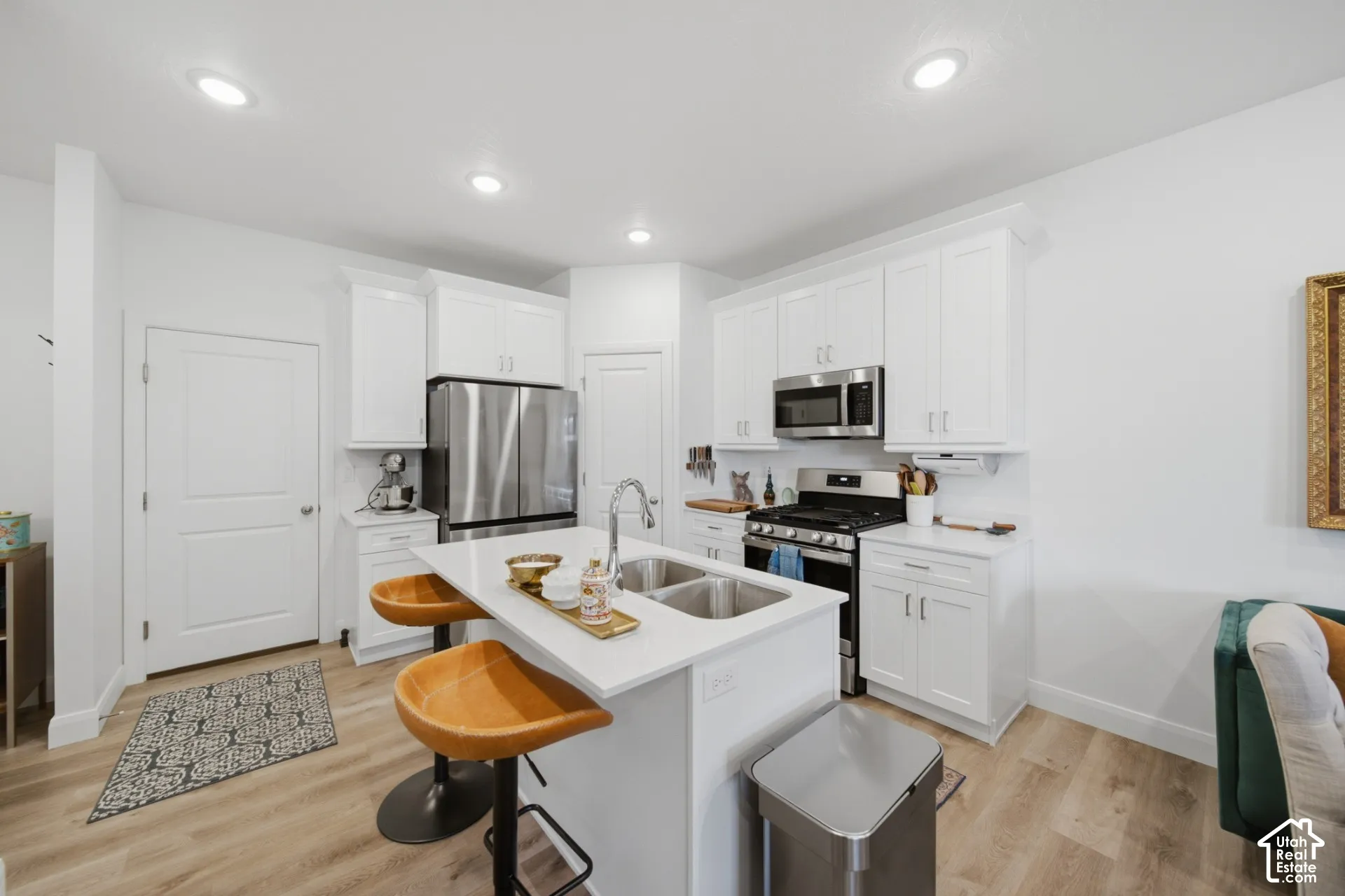 Kitchen featuring white shaker-style cabinetry, quartz countertops, a central island with a double-basin stainless steel sink, wood-finish flooring, and recessed lighting