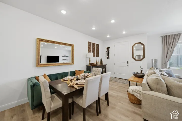 Neutral color palette featuring light-toned wood-finish flooring, crisp white walls, recessed ceiling lighting, and a paneled entry door