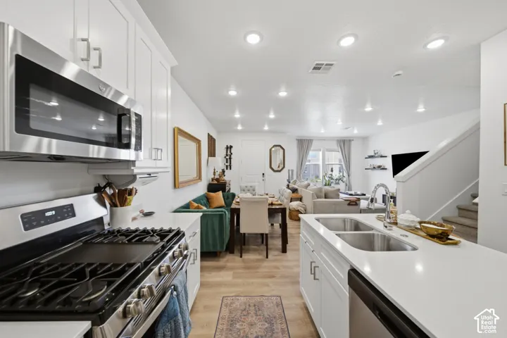 Kitchen featuring white cabinetry, stainless steel appliances, a center island with a double-basin sink, quartz countertops, and wood-finish flooring