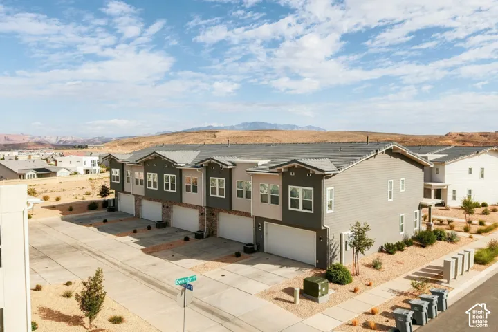 Multi-level residential exterior featuring horizontal siding, multi-gabled rooflines, attached garages, and a backdrop of desert mountain topography