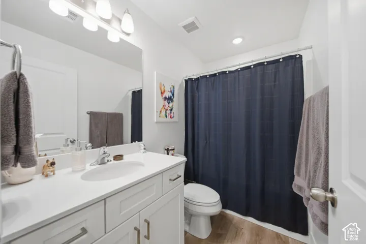 Bathroom featuring a white vanity with a solid-surface countertop, an integrated oval basin, polished chrome hardware, and wood-finish flooring