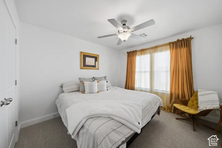 Neutral-toned wall-to-wall carpeting, ceiling fan with integrated lighting, dual-panel interior door with brushed nickel hardware, and multi-pane window with horizontal blinds