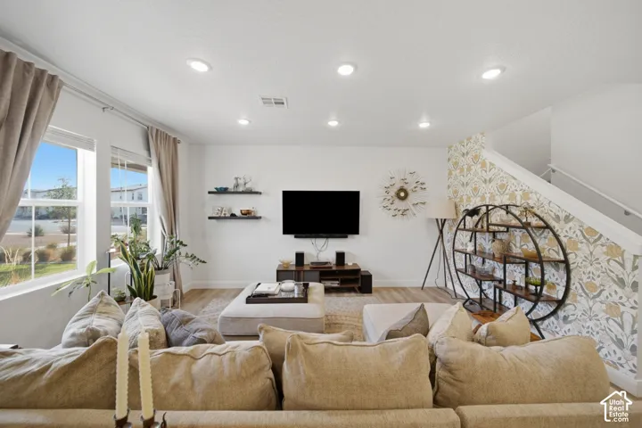 Living area featuring recessed lighting, wood-finish flooring, two floating shelves, and an accent wall with patterned wallpaper